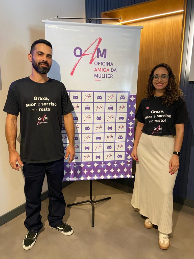 Raphael e Rafaela no encontro em Joinville/SC Imagem que mostra os proprietários da oficina Poa Car Service em frente ao banner do evento na cidade de Joinville/SC